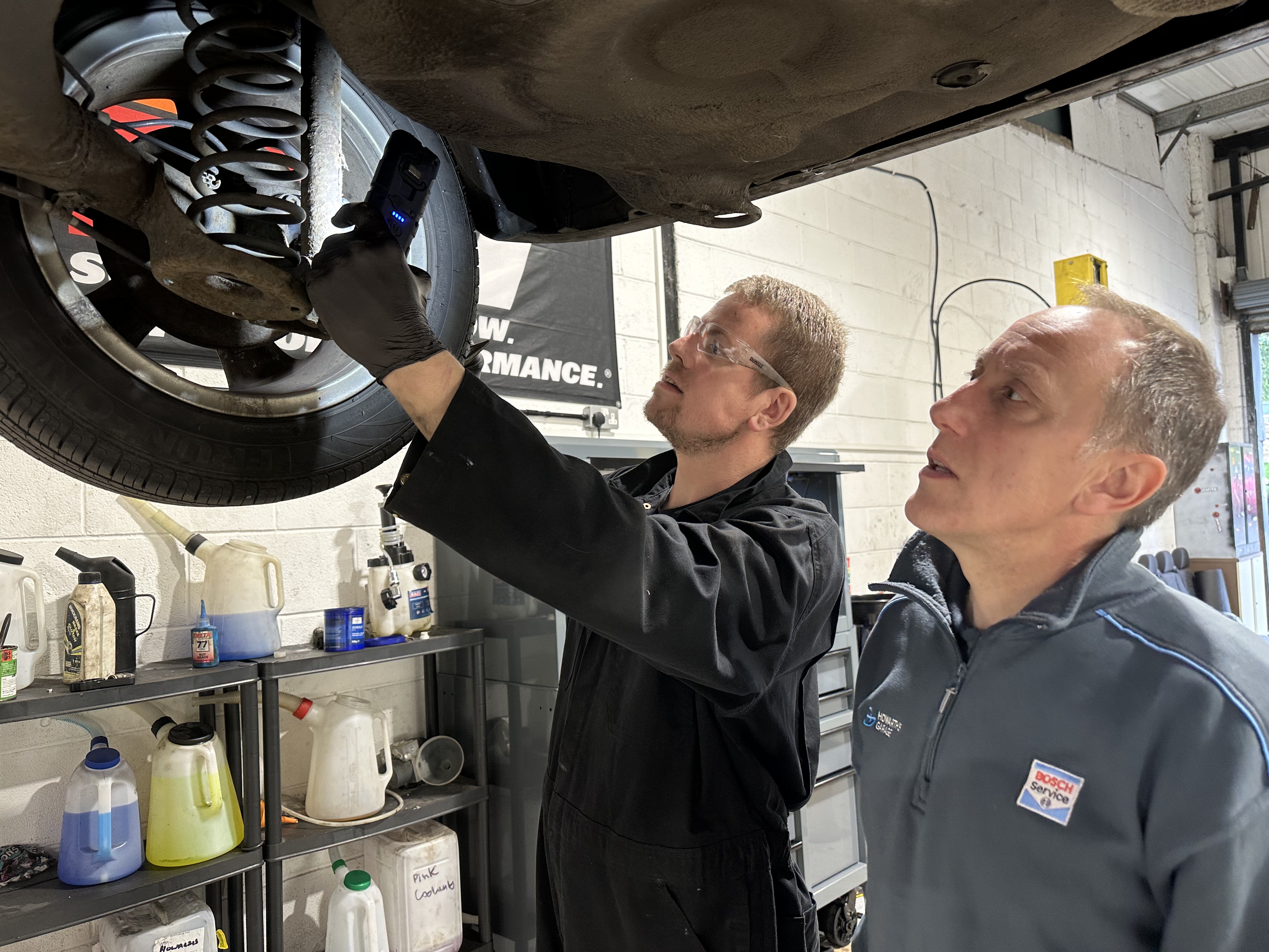 Howarths Garage - EV Servicing - Image of owner Phil and one of his mechanics looking at the wheel of a car up on the ramp